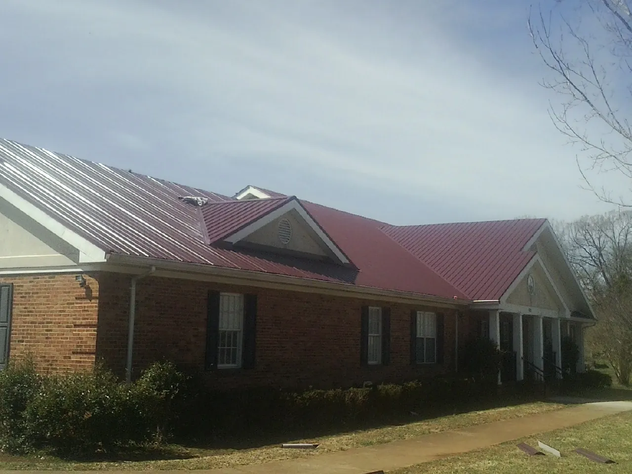 Red metal roof with gabled entries on a long brick building, from a Hail Damage Roof Repair job in Nine Mile Falls