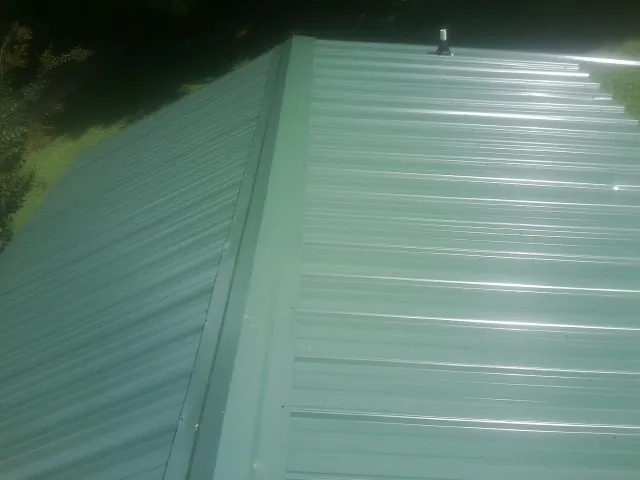 New green metal panels meeting at the ridge of a roof — Flat Roof Repair work by our crew in Nine Mile Falls
