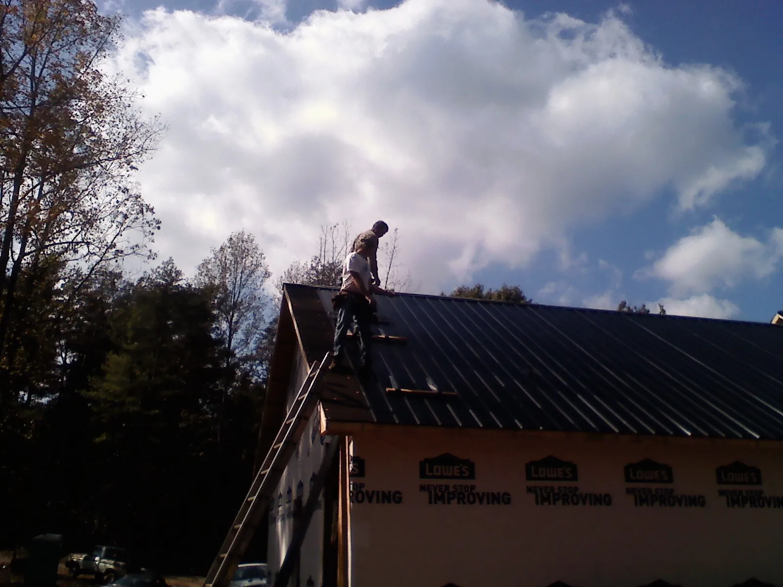 Roofer fastening dark metal panels high against a cloudy sky, from a Roof Inspection job in Nine Mile Falls