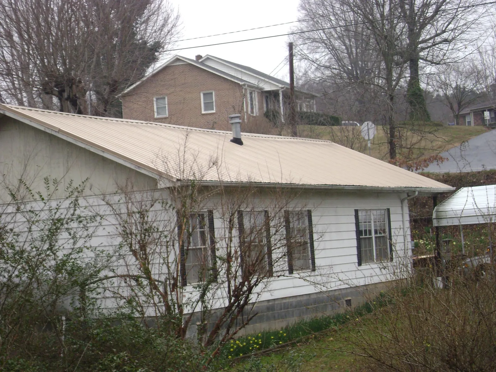 Tan metal roof on a white sided house set into a hillside — Commercial Roofing by Roofing Brothers in Nine Mile Falls