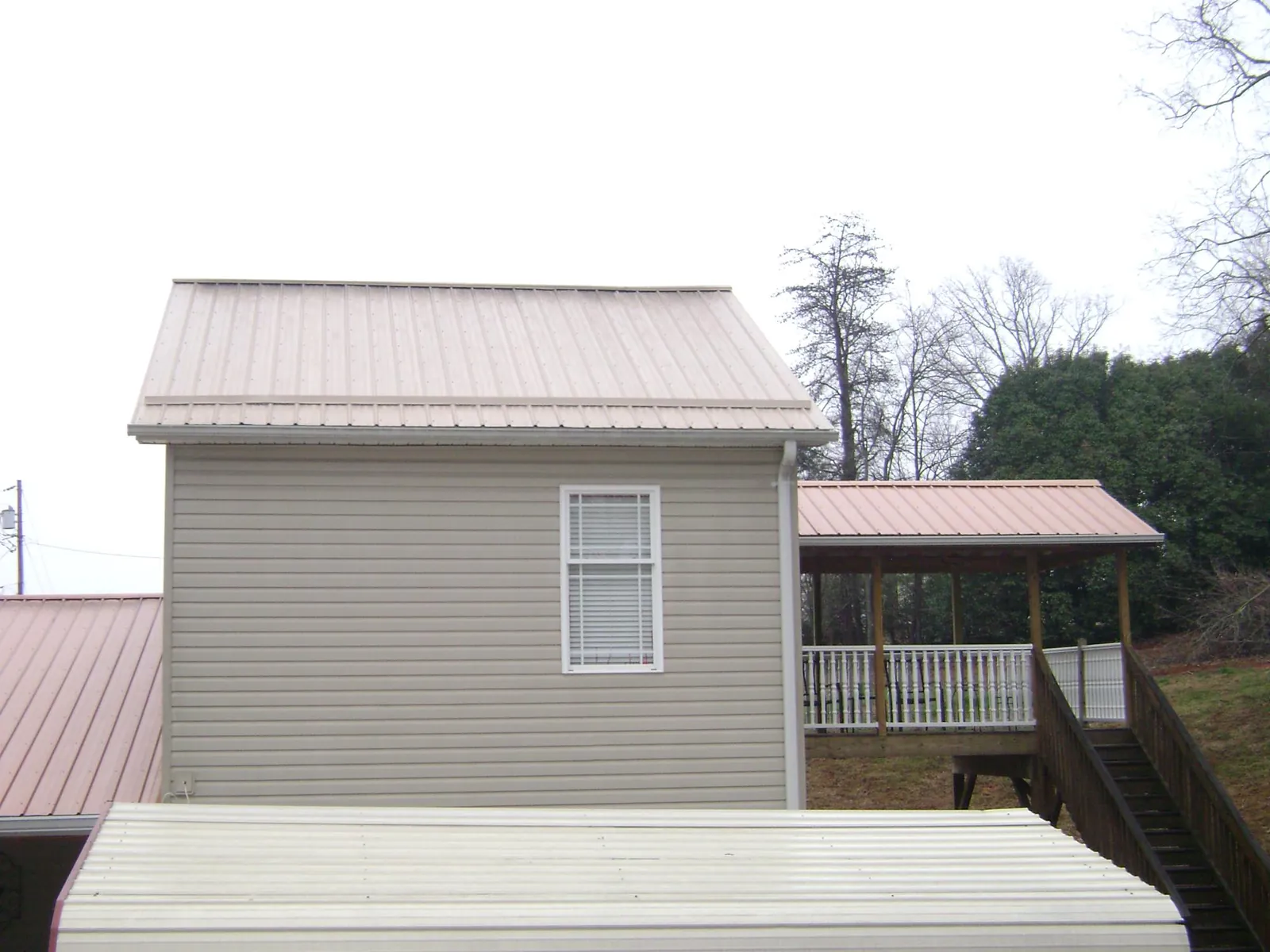 Tan metal roofs on a two story addition and attached porch, from a Roof Replacement job in Nine Mile Falls